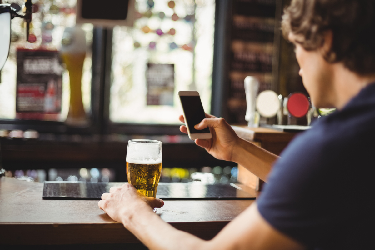 Homem com um celular, bebendo cerveja, enquanto compra cervejas online.